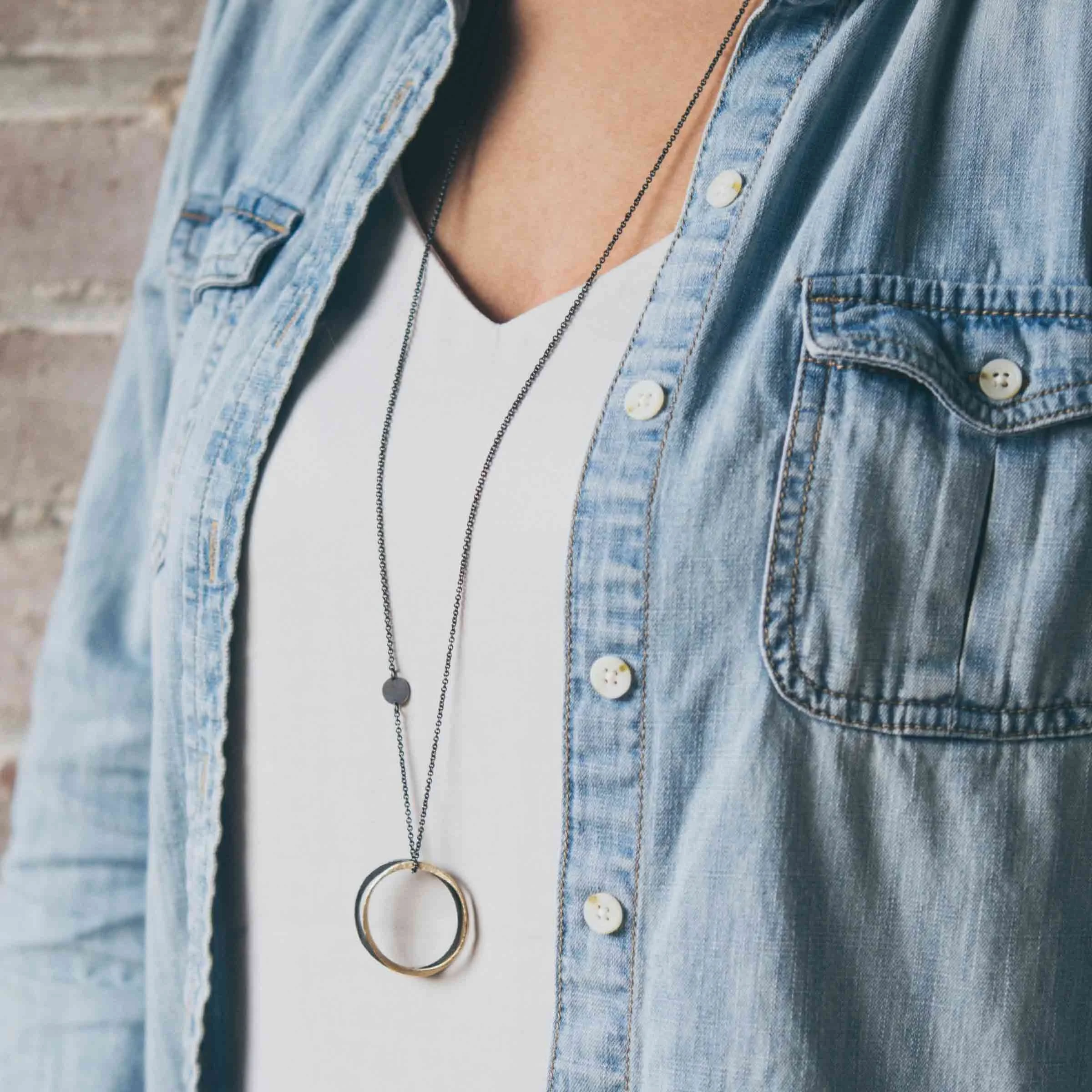 Model wearing the patinated sterling silver and gold crossover circle necklace styled as a long-line statement pendant.