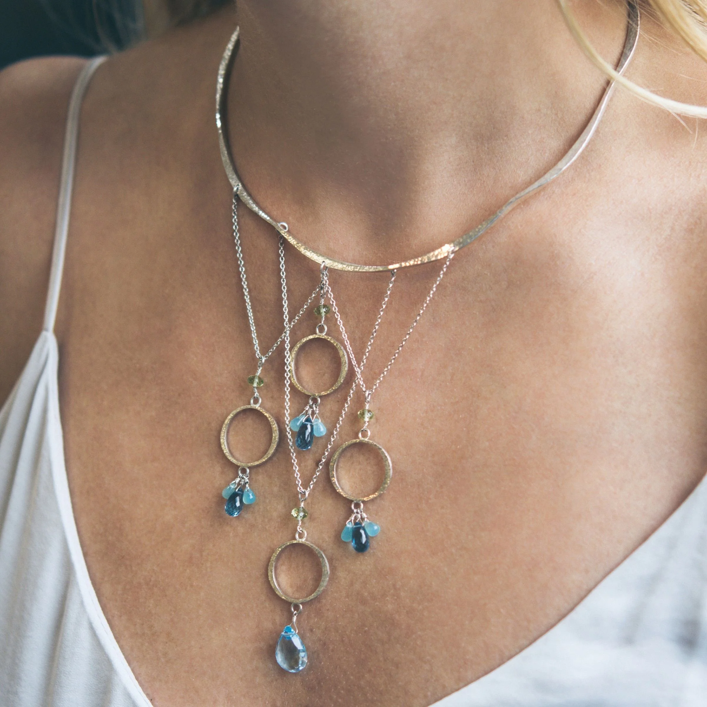 Close-up detail of wire-wrapped peridot, Peruvian opal, London blue topaz, and Swiss blue topaz gemstones on a hand-textured sterling silver festoon necklace
