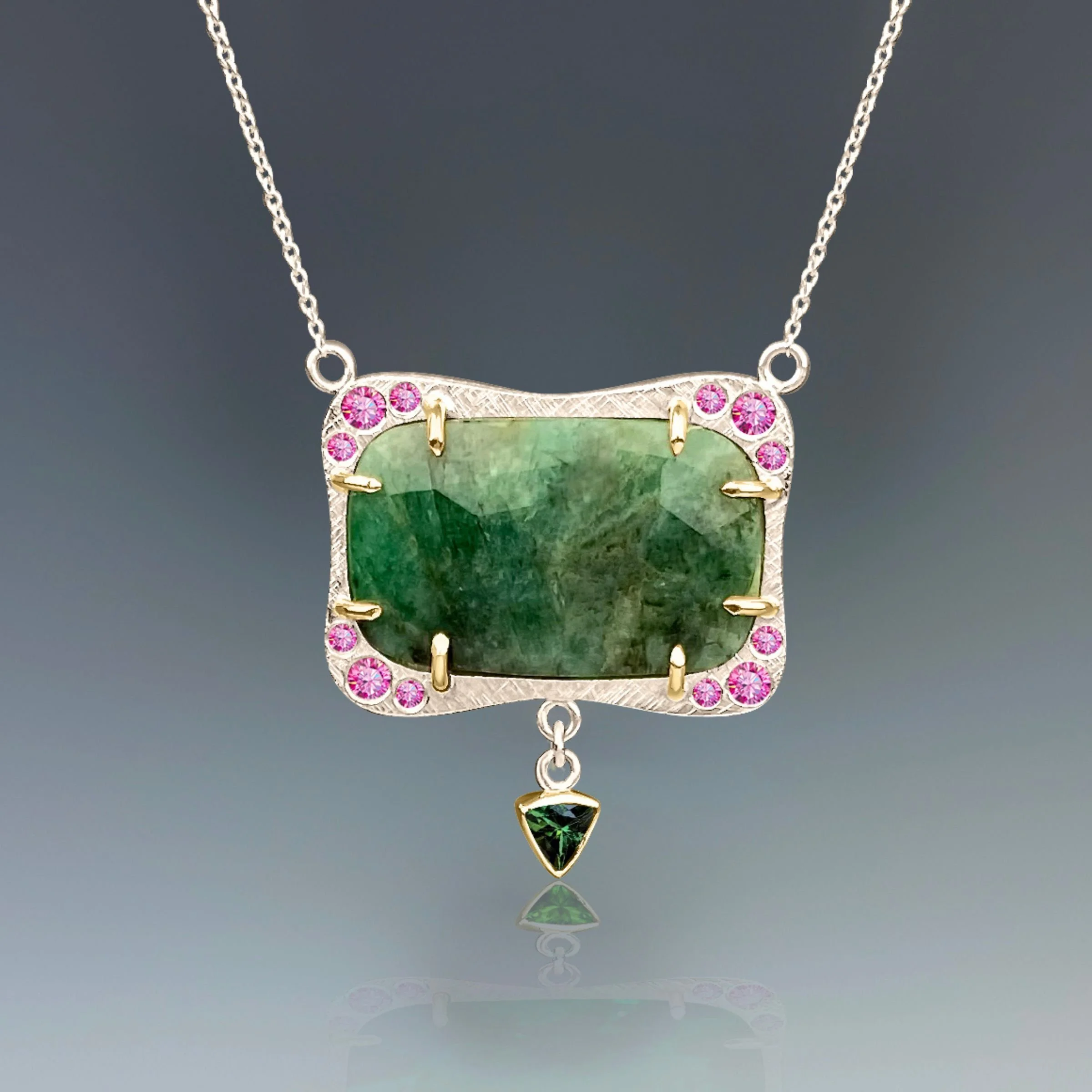 Detail view of the EatMetal emerald and pink sapphire deco frame pendant showing the gold prong settings, sterling silver chain, and green tourmaline drop.