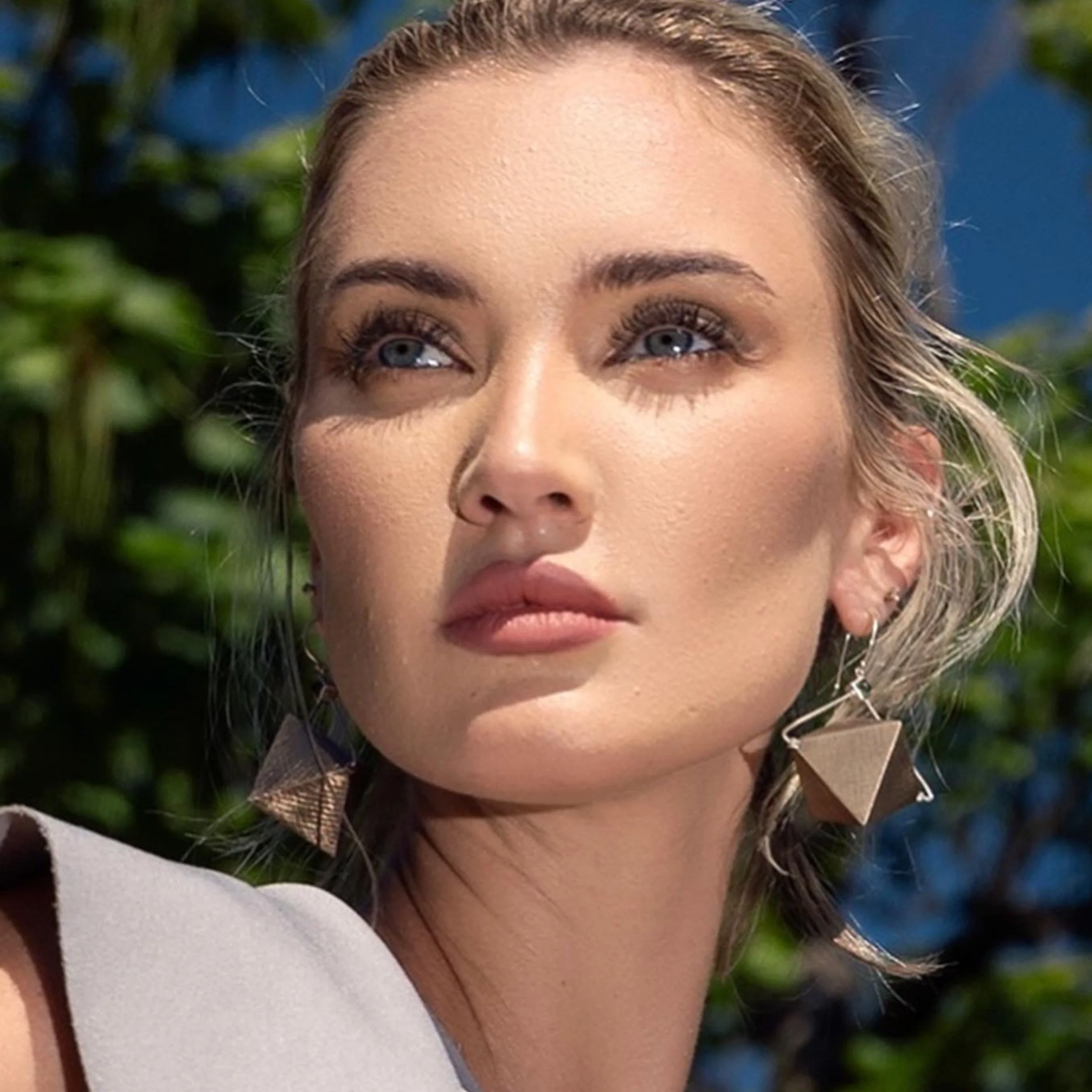 Model wearing the EatMetal sculptural bronze and sterling silver octahedron pyramid dangle earrings with green tourmaline.