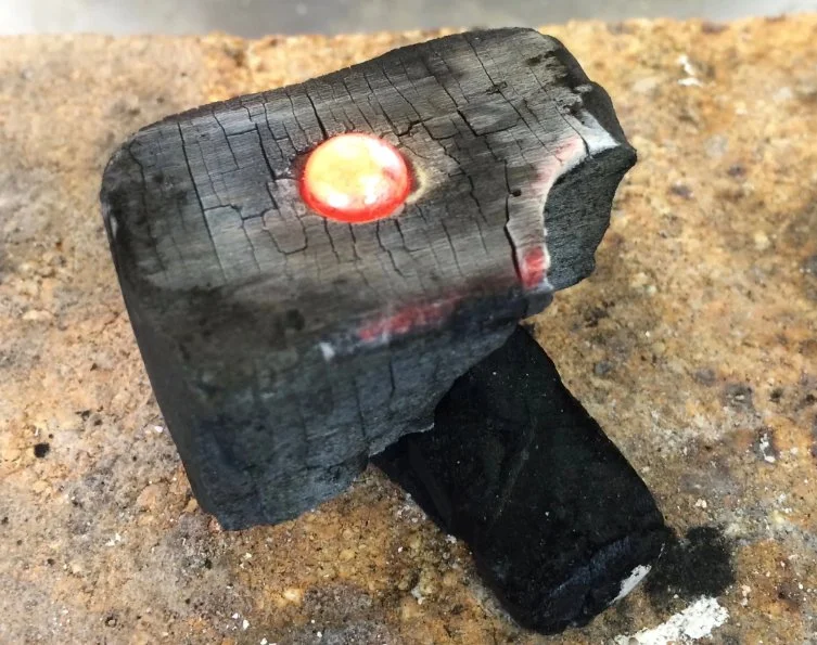 melted metal ingot on black charcoal block ready for hand fabrication