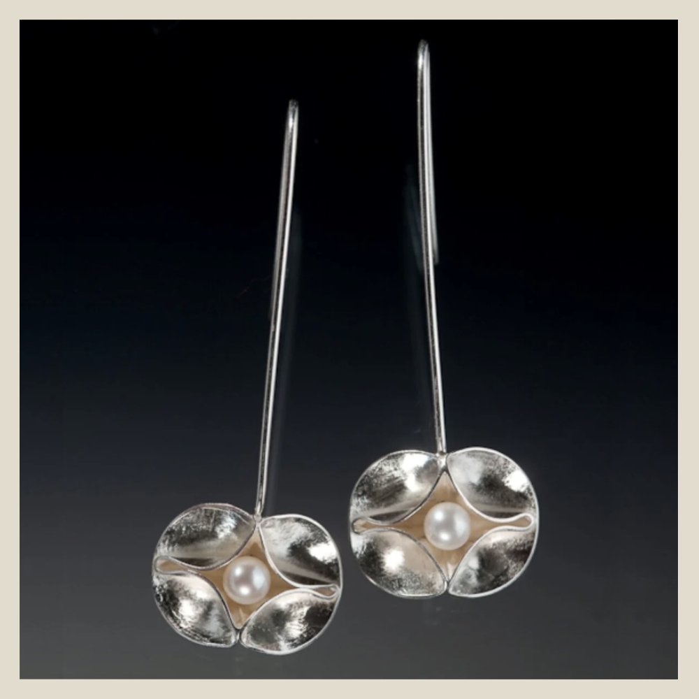 Silver earrings with pearl centers and petal-like designs against a dark background.