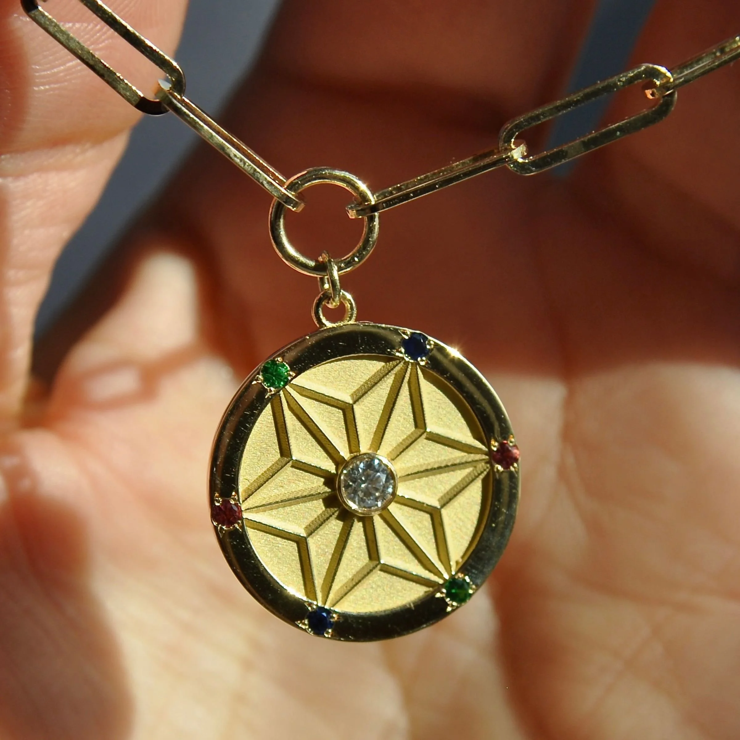 engraved geometric star pattern 14k yellow gold- Asanoha Japanese diamonds, 6 pointed starburst medallion pendant featuring a central round diamond accent and a polished border set with sapphires, emeralds, and rubies on an open-link paperclip chain