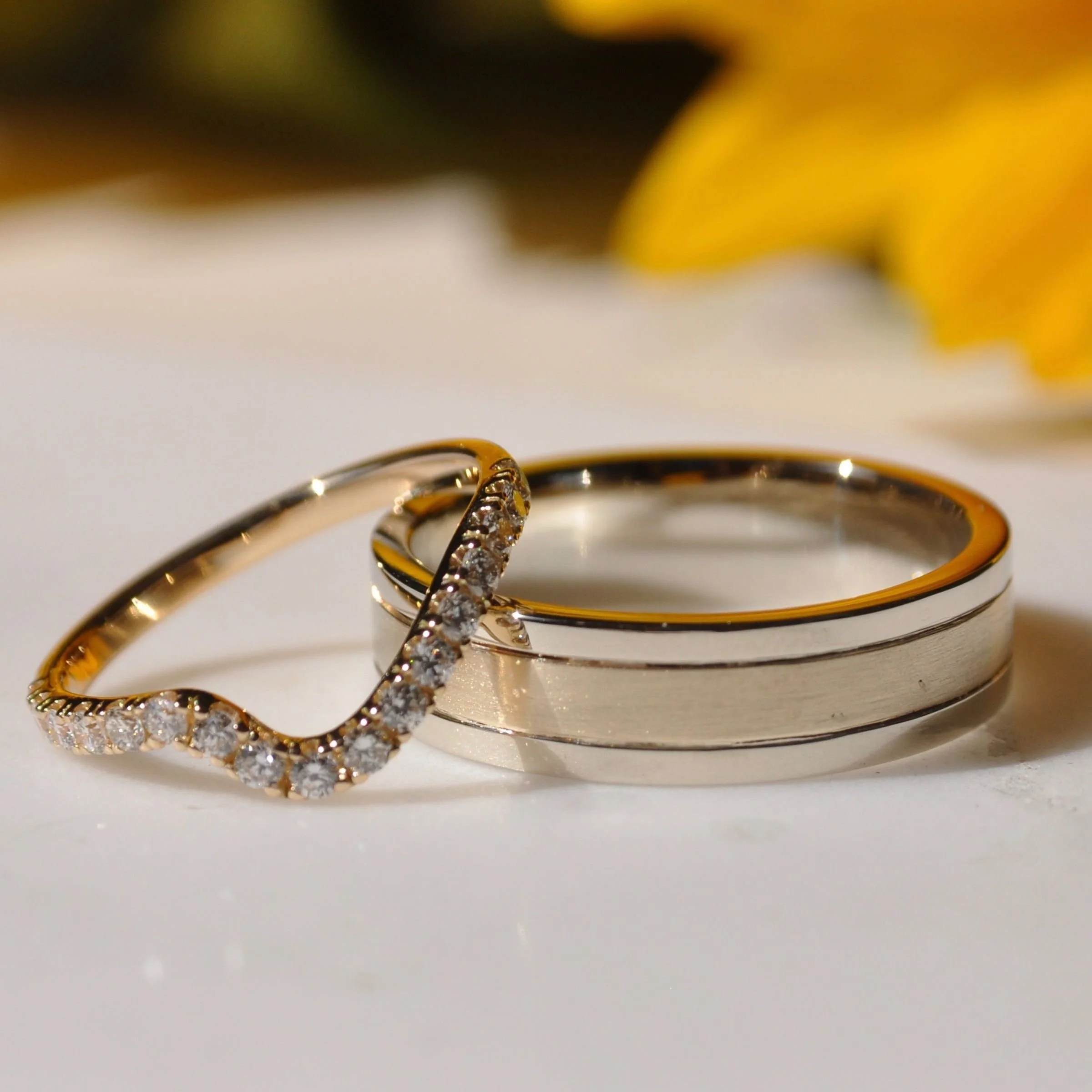 A modern wedding ring set featuring a thin contoured 14k yellow gold diamond pavé-set band and a wide men's bi-colored 14k yellow and white gold band with a matte brushed finish.
