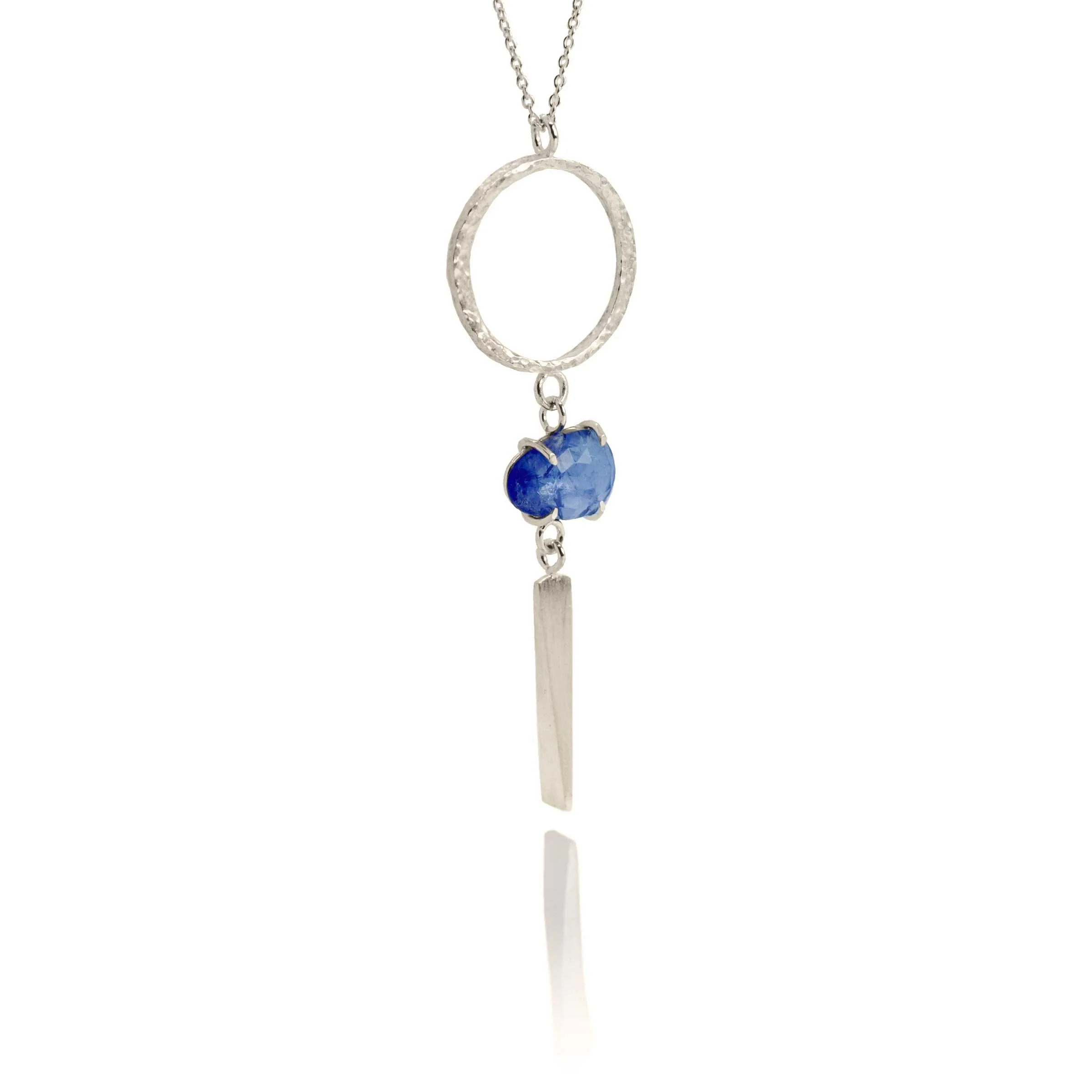 Close-up detail of a vibrant rose-cut gemstone set between a forged silver circle and drop bar pendant