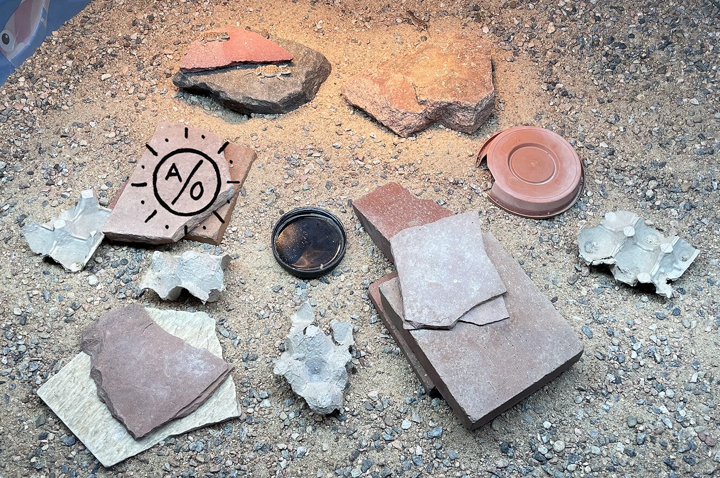 Various pieces of flat and cracked bricks and stones, some with markings, on a gravel surface