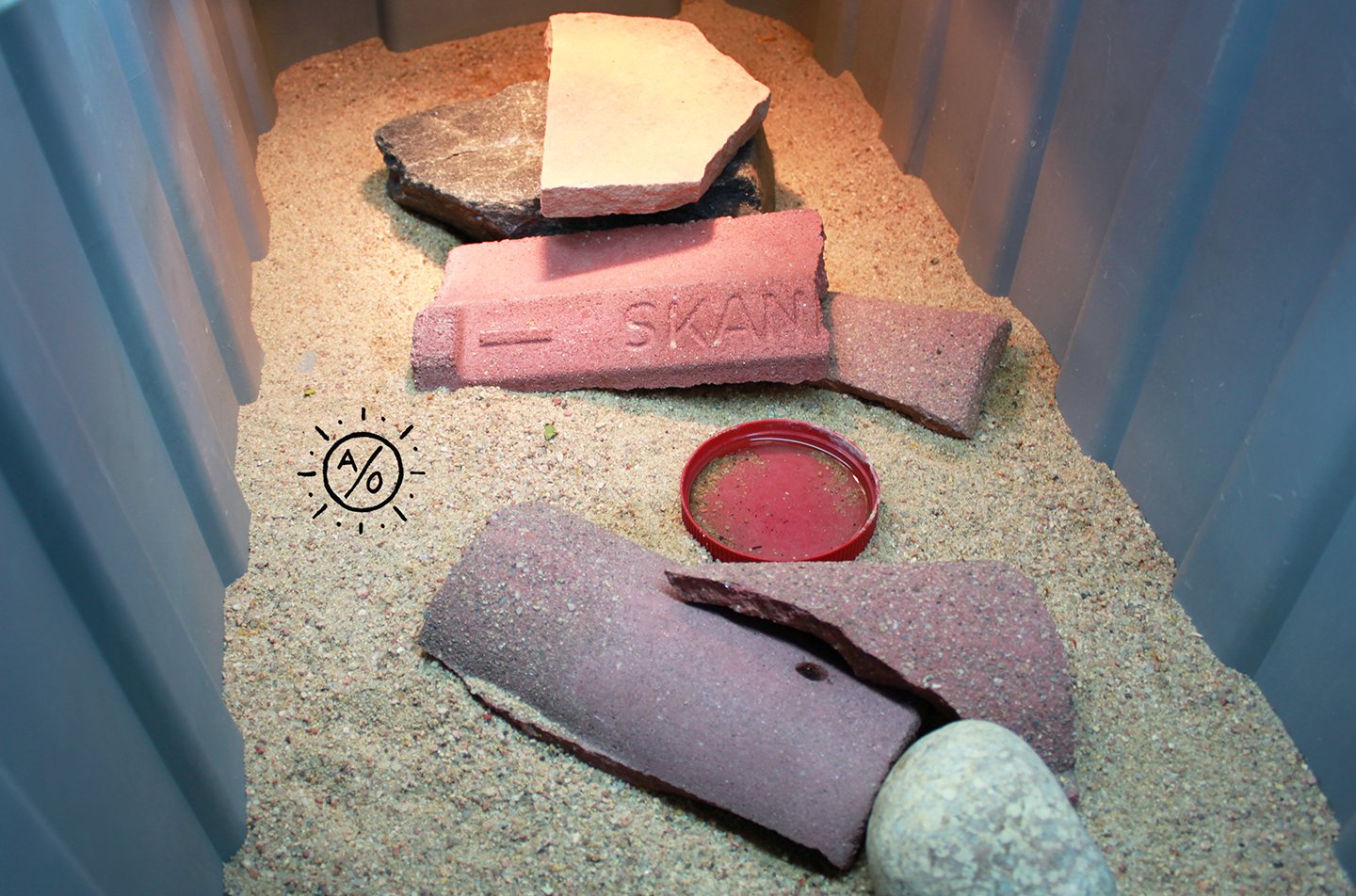 Sand-filled container with various bricks and stones arranged inside.