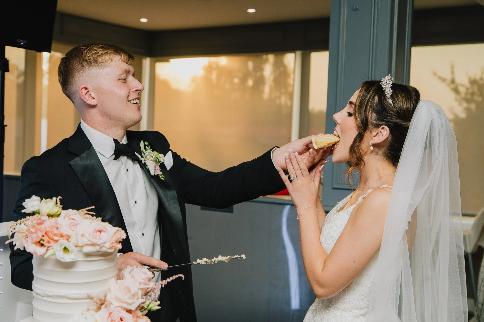 A happy couple on their wedding day eating cake at Skylark Country Club in hampshire, they are stood in front of a sunset.