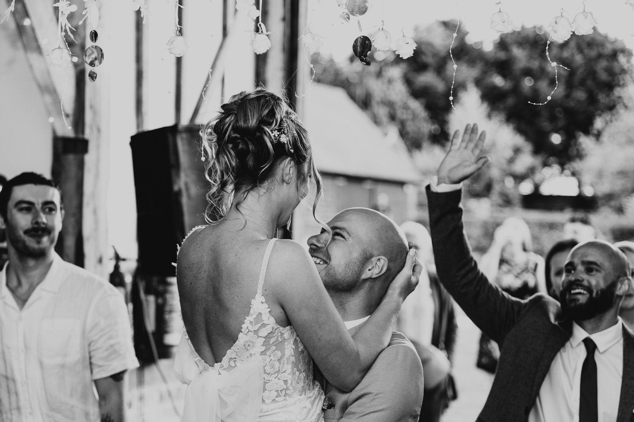A woman in a wedding dress and a man in a suit share a joyful moment at a wedding reception, with friends celebrating around them.