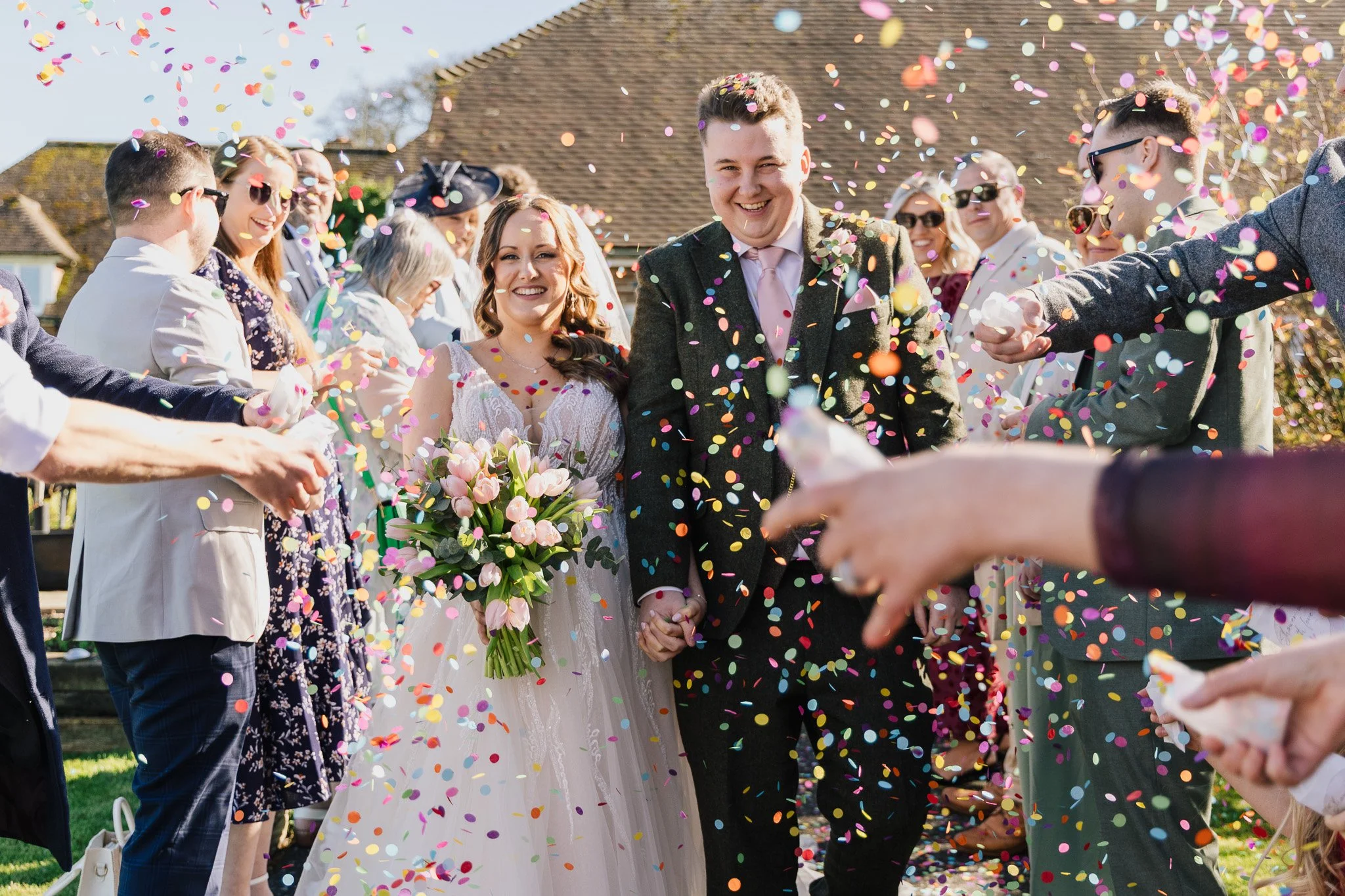 A happy couple on their wedding day, walking, being showered in confetti, at Wickham Estate, Hampshire.