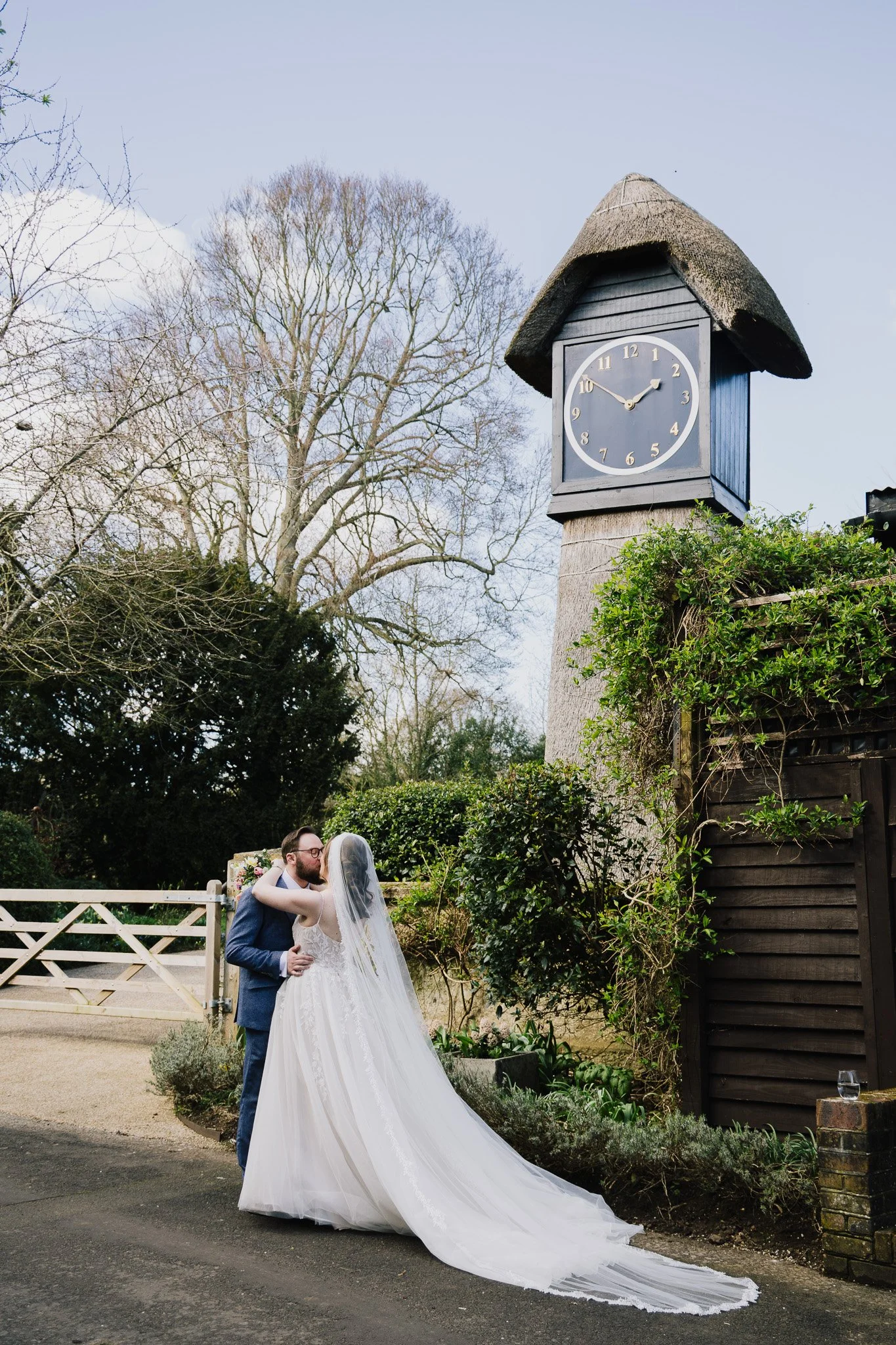 A happy couple on their wedding day, in front of a clock, at Clock Barn, in Hampshire.