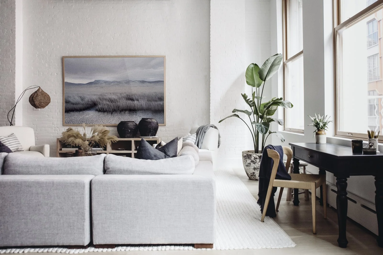 The airy living room shows off a monochrome landscape by Petros Koublis framed by an Interior Define sectional and Verellen coffee table. Extra accents include a floor lamp by Bungalow Decor in Westport, block print pillows by Susan Connor, aerrain plant pot, and black urns by Habitat Greenwich. Tying the space together is a rug from Restoration Hardware. (Chloe Leroux)
