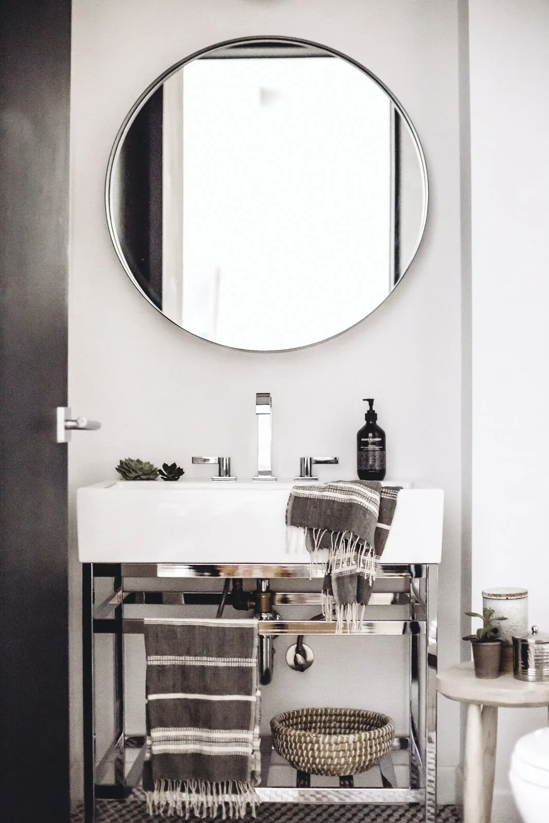 The stone-hued palette makes its way into the powder room where minimalist style is matched with luxurious textiles from Creative Women and silver finishings. A Pottery Barn vanity offers a foundation for a Dornbracht faucet and Grown Alchemist soap. (Chloe Leroux)