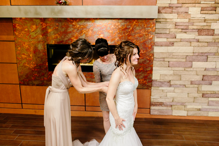 Bride and mothers helping her into her wedding gown on her wedding day