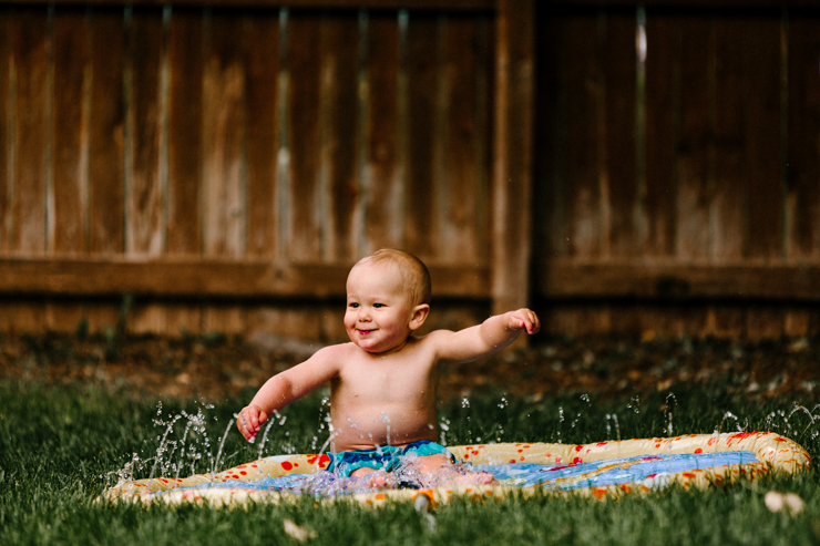 One year old baby boy playing in the water in his backyard