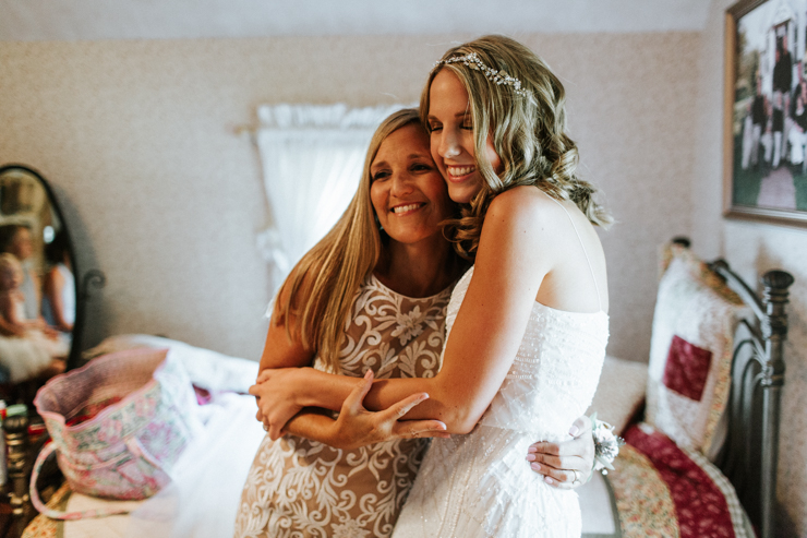 Bride getting ready for her wedding and hugging her mother, both wearing BHLDN Wedding Gowns