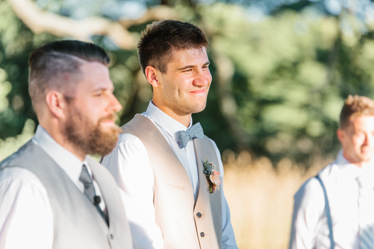 Groom as he sees his bride walk down the aisle for the first time at outdoor ceremony at grandparents' farm