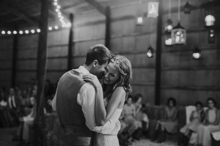 Bride and Groom dancing under edison bulbs and chandeliers in a beautifully decorated barn
