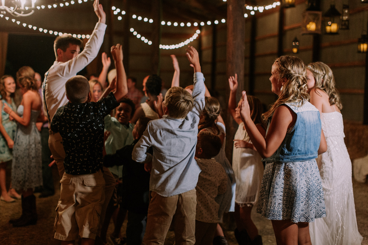 Bride, groom, and friends dancing at midwest barn reception lit with edison bulbs