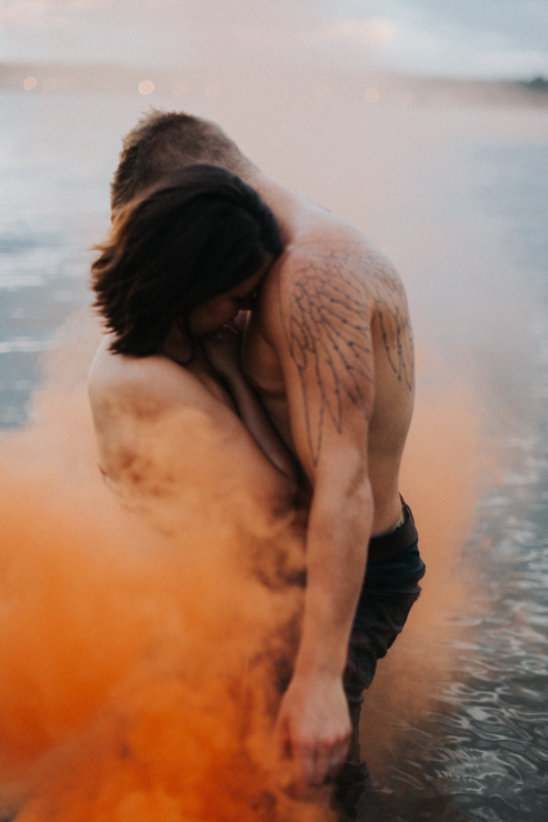 Intimate couple photography nude in the water with an orange photography smoke bomb 