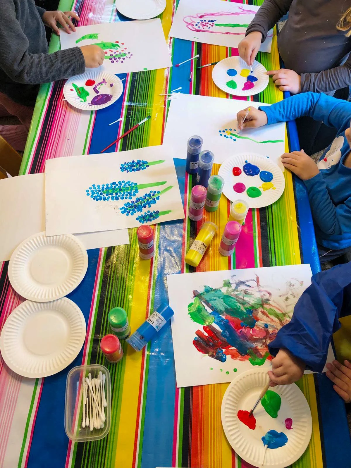 Kinderwerkstatt students creating colorful paintings with paint and cotton swabs.