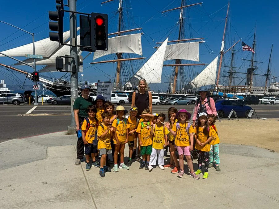 Group of summer camp participants posing in front of a tall ship docked at a harbor.