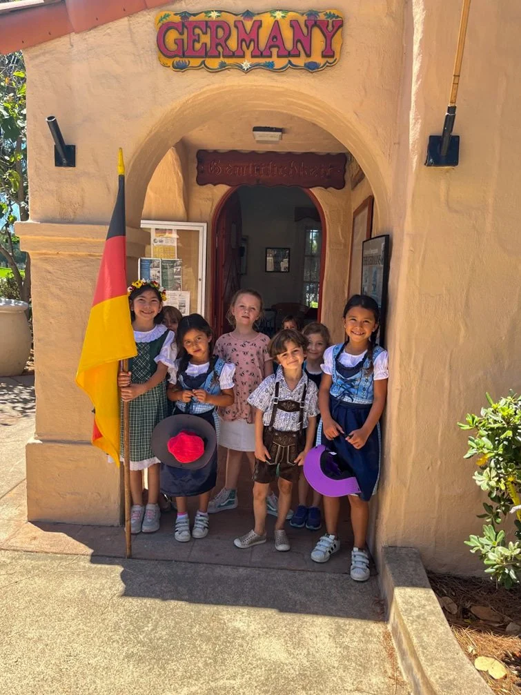 Children dressed in traditional German costumes standing in front of the House of Germany cottage.