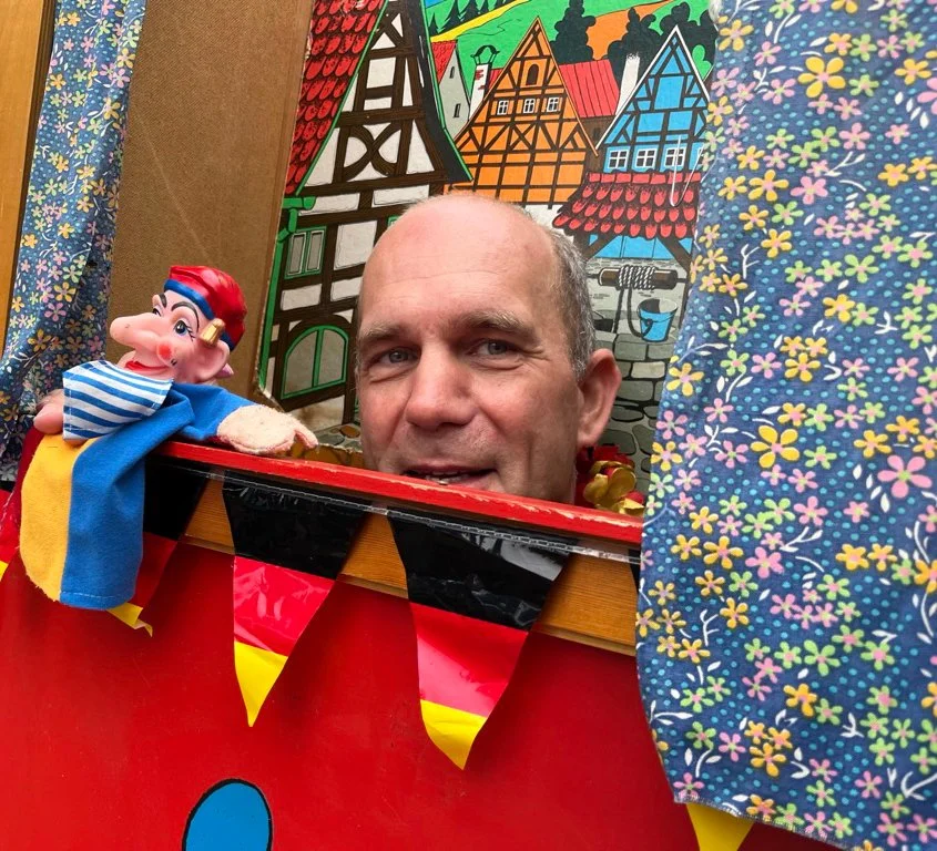 Close-up of man holding a puppet looking through a puppet theater stage.
