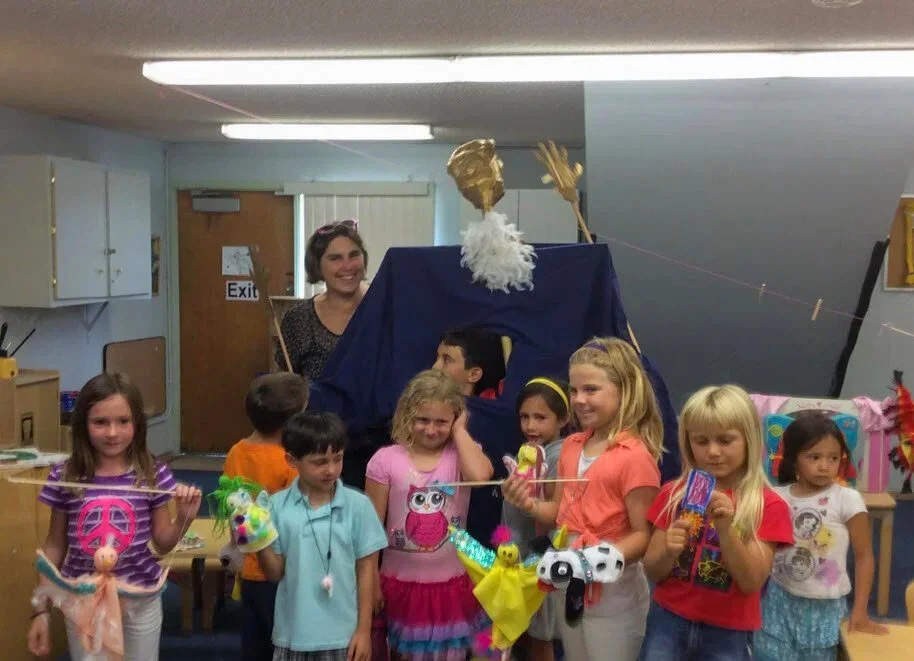 Kinderwerkstatt students posing with their teacher, holding hand-made puppets.
