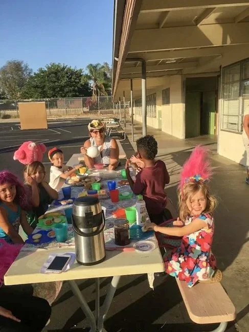 Kinderwerkstatt students having lunch with their teacher at a picnic table.
