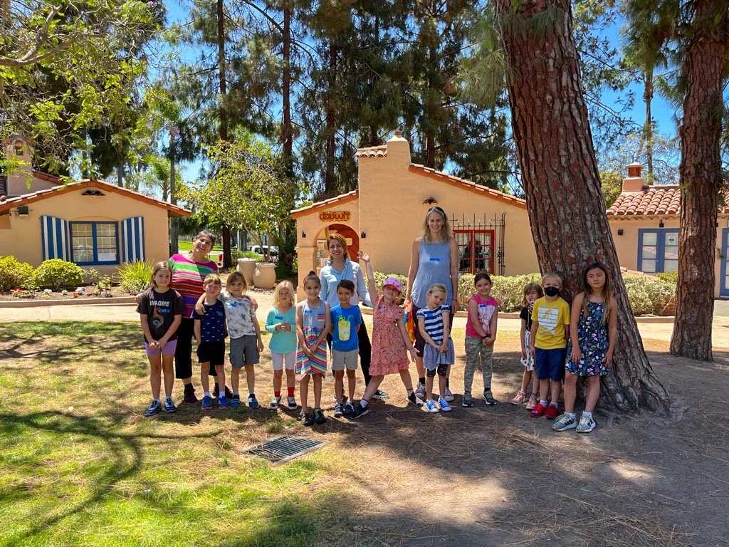 Group of Kinderwerkstatt students and their teachers posing in front of the House of Germany cottage.