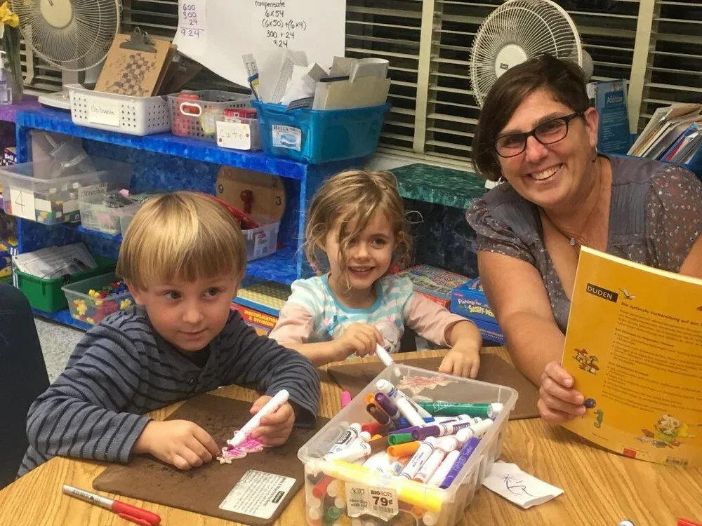 Two Kinderwerkstatt students sitting at a table with their teacher.