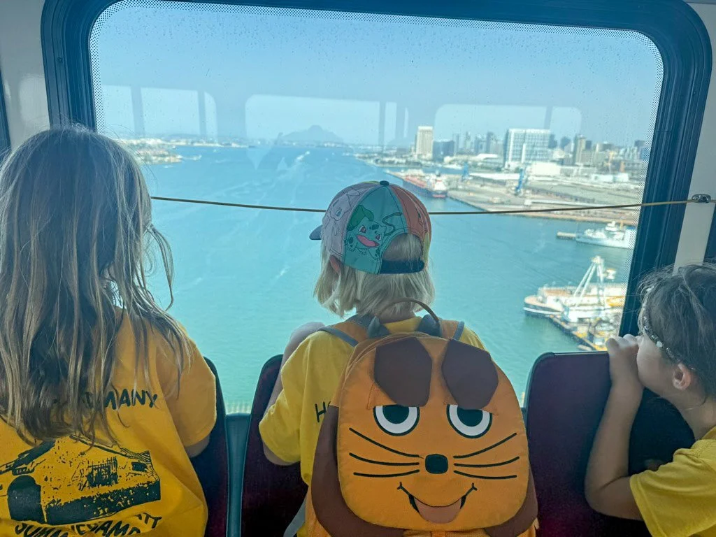 Three summer camp participants looking out a large window at a city skyline and waterway.
