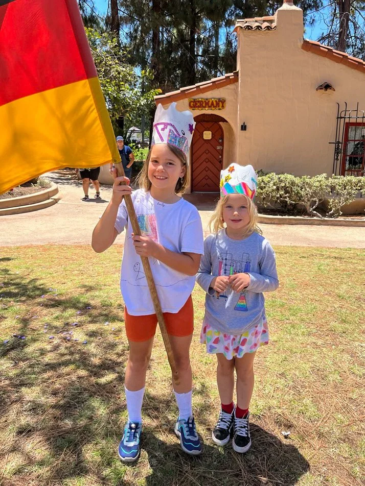 Two Kinderwerkstatt students wearing crafted crowns and holding the German flag.