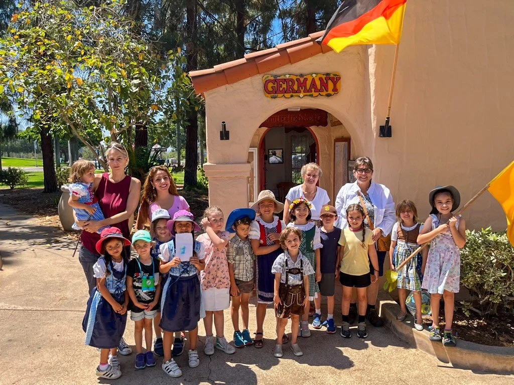 Group of Kinderwerkstatt students posing with their teachers in front of the House of Germany cottage.