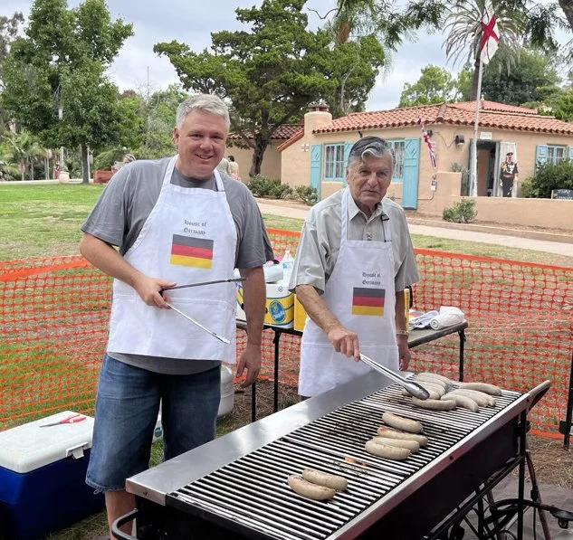 Two House of Germany members grilling sausages at a past lawn program.