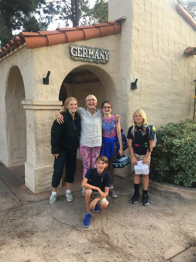 A group of Kinderwerkstatt students posing with their teacher in front of the House of Germany cottage.