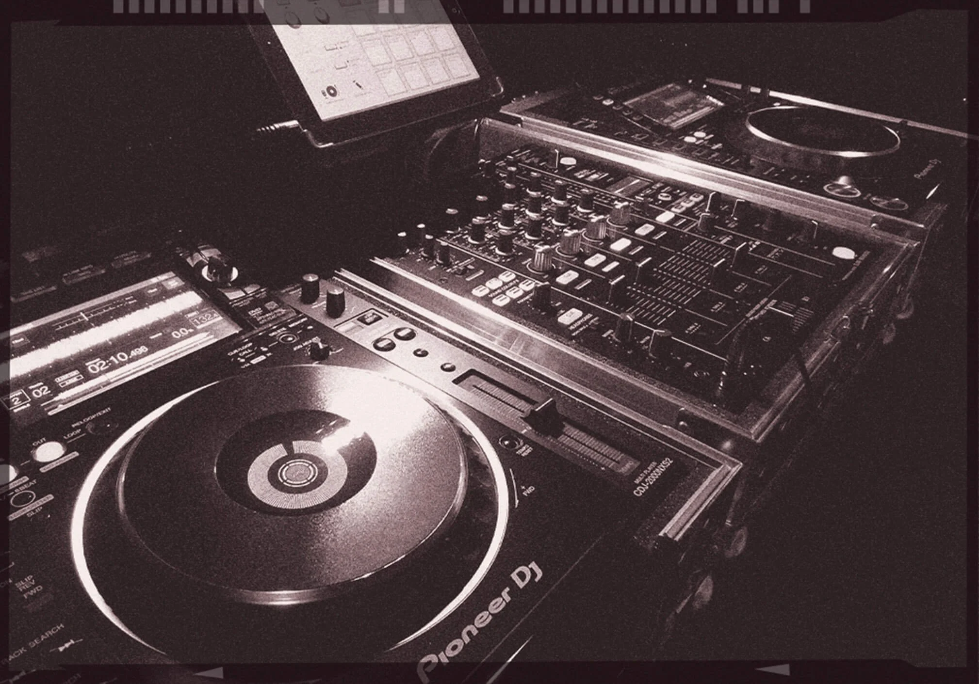 DJ equipment including a Pioneer DJ controller, a mixer, and a screen displaying music tracks.