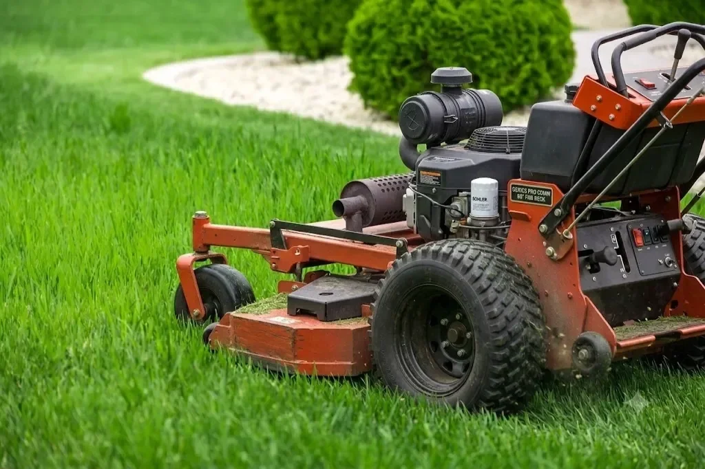 Commercial walk-behind lawn mower cutting lush green grass along a manicured residential lawn landscape.