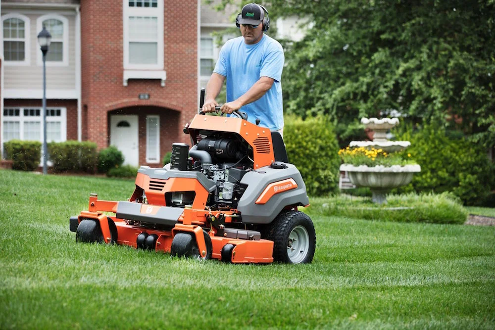 A professional landscaper operating an orange stand-on commercial mower to create clean stripes on a green residential lawn.