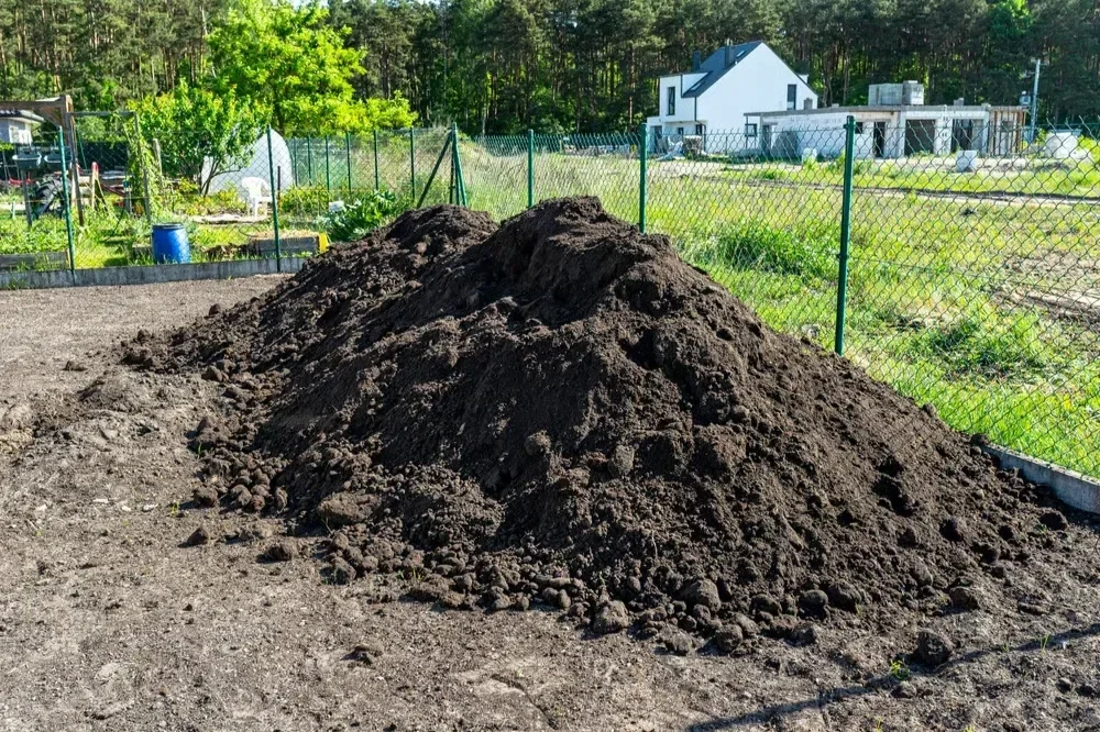 Large pile of dark, rich organic topsoil and mulch delivered for a residential landscaping lawn installation.