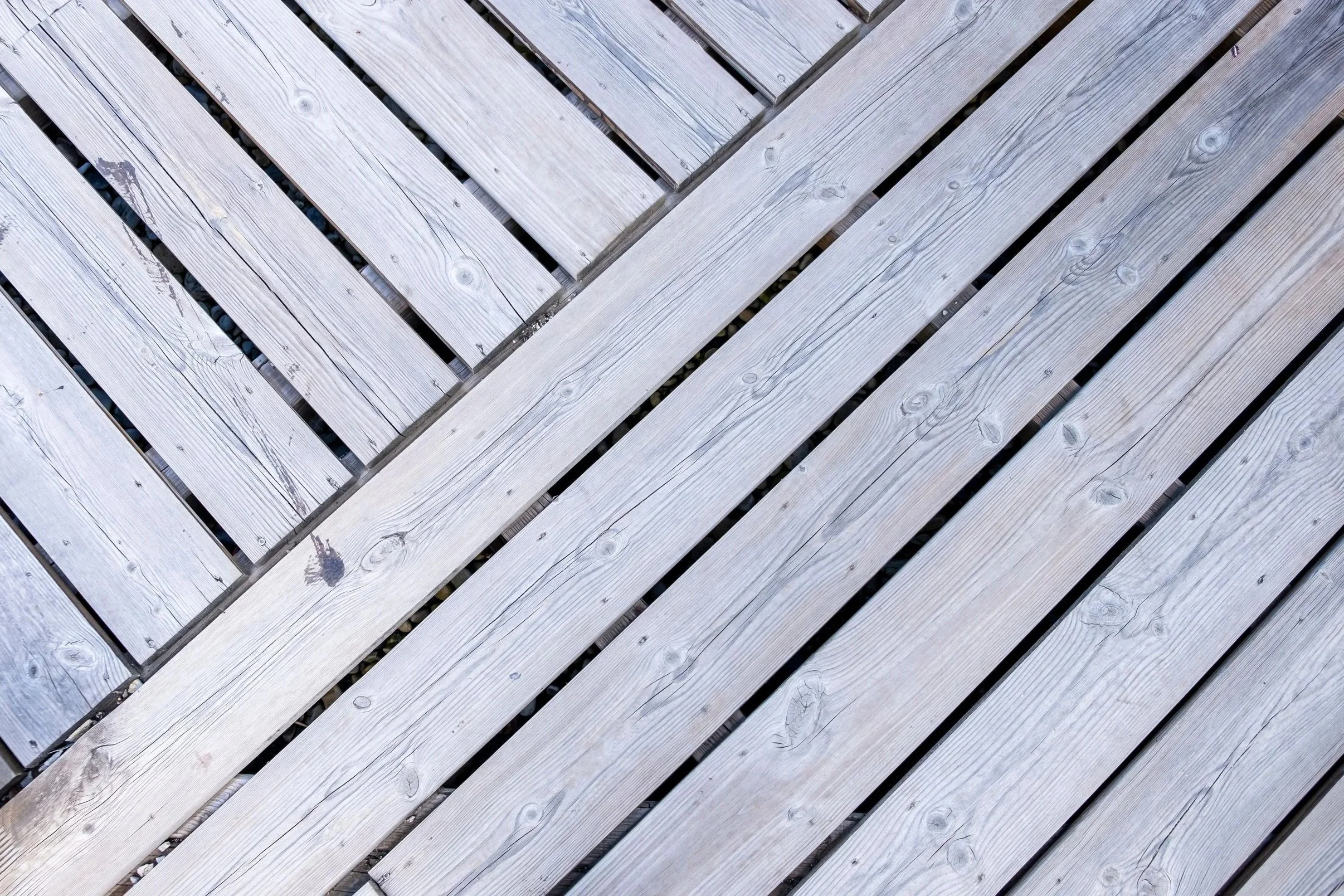 Overhead view of a wooden deck featuring light gray weathered planks arranged in a decorative diagonal pattern.