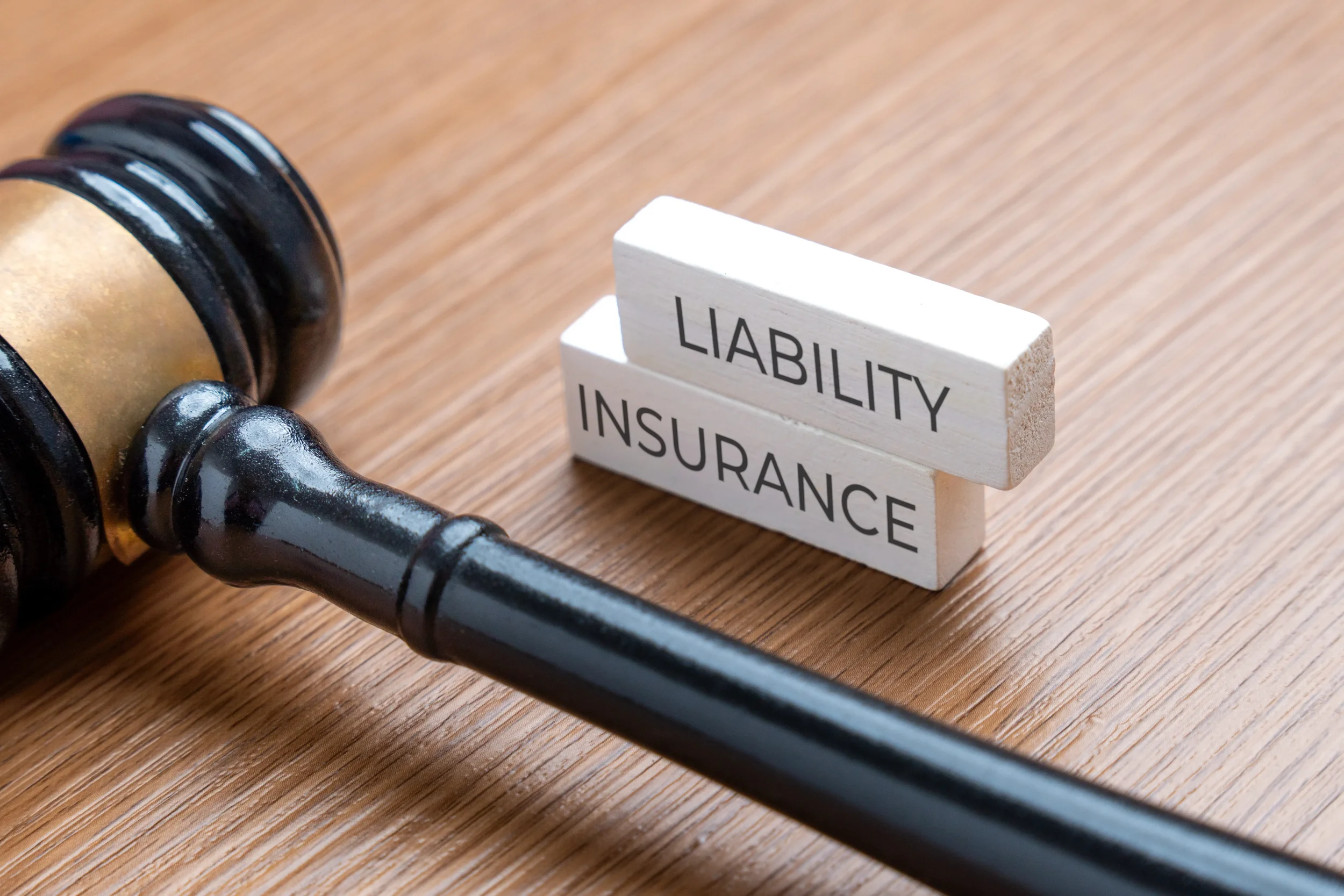 A wooden judge's gavel resting next to white blocks that read Liability Insurance on a wooden desk.