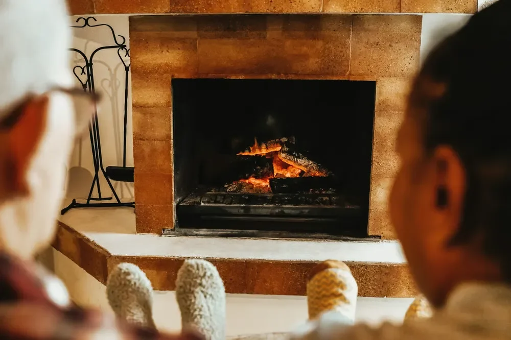 Two people wearing cozy socks relaxing and warming their feet by a burning wood fireplace.