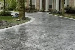 Elegant winding driveway featuring gray stamped concrete with a textured slate finish and light-colored stone borders.