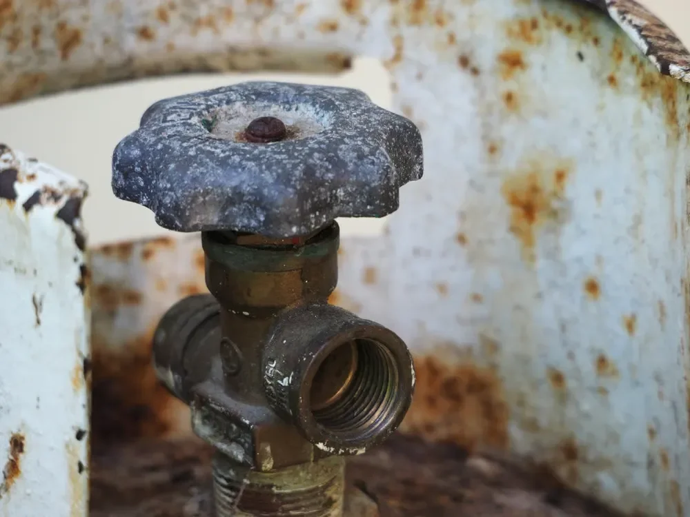 Close-up of a rusty propane tank valve on an old, weathered gas cylinder.