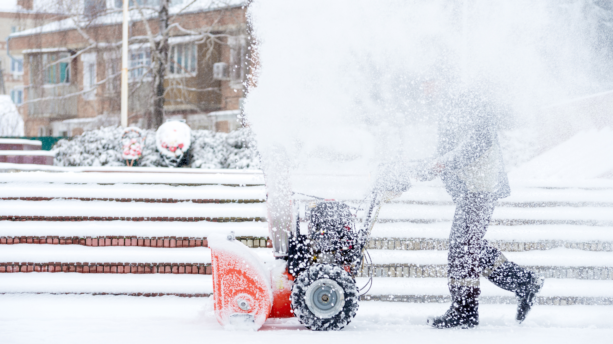A professional using a powerful snow blower to clear deep snow from outdoor stairs in a commercial area.