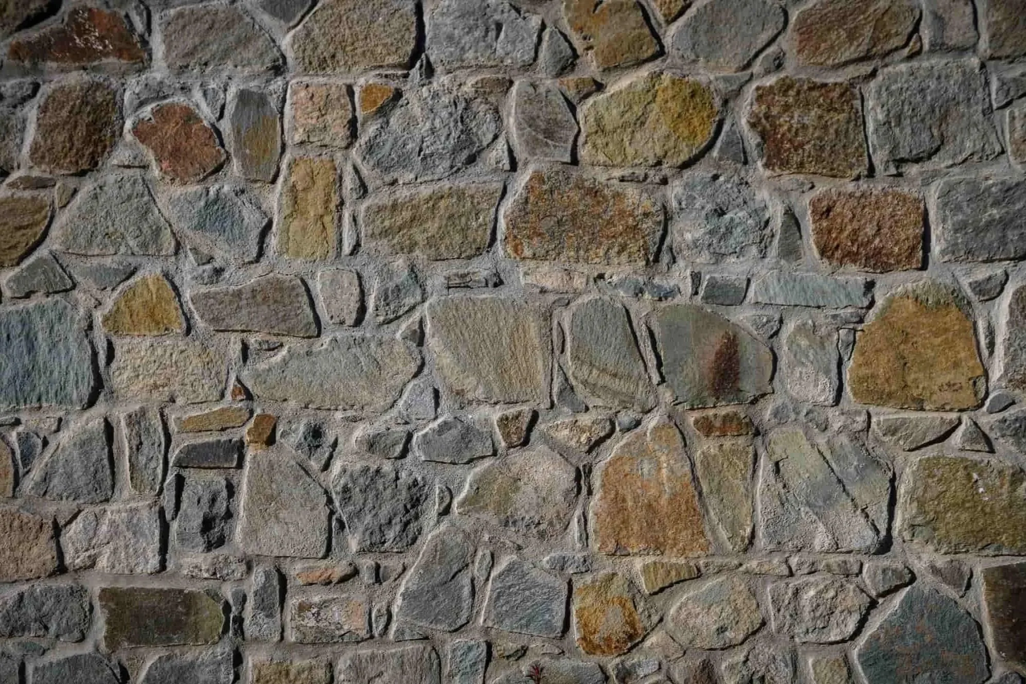 Close-up of a rustic mosaic fieldstone wall featuring earth-toned stones in various shades of brown, gold, and gray.