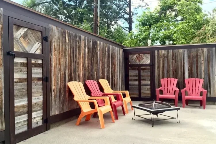 Rustic wooden privacy fence and patio with colorful chairs and a fire pit.