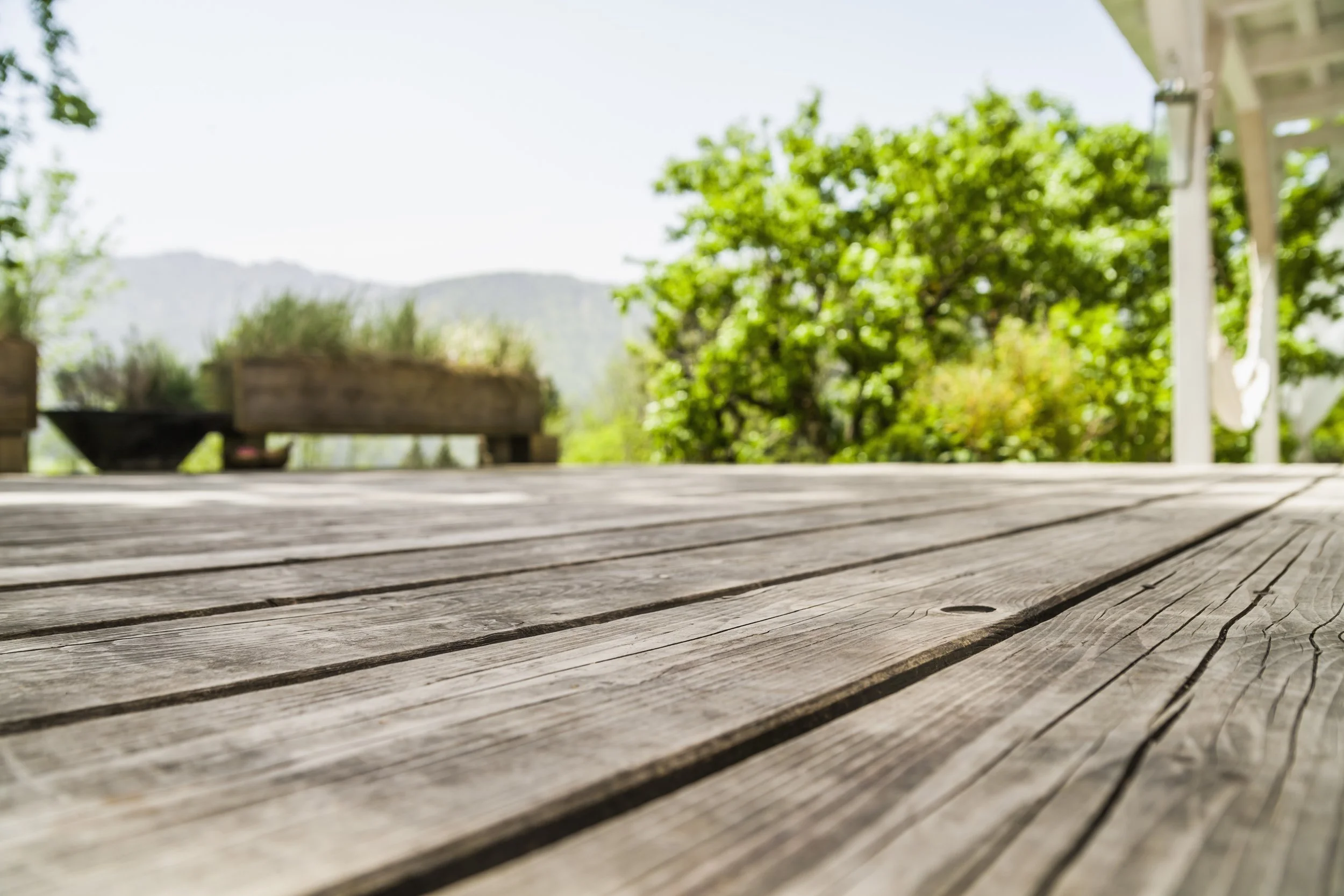 Low-angle view of a rustic wooden deck with a blurred background of a lush garden and mountains.
